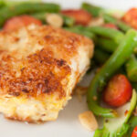 A blackened basa filet on a dish with asparagus and cherry tomatoes