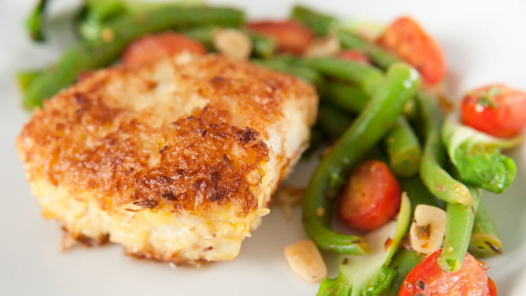 A blackened basa filet on a dish with asparagus and cherry tomatoes